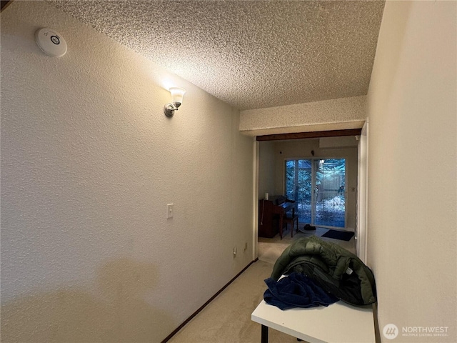 corridor featuring a textured ceiling, a textured wall, and light carpet