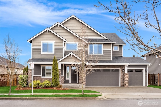 craftsman-style home with a front yard, fence, roof with shingles, concrete driveway, and stone siding