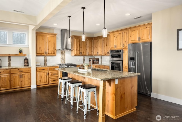 kitchen with wall chimney range hood, light stone countertops, visible vents, and appliances with stainless steel finishes