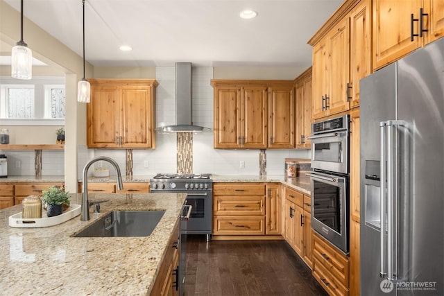 kitchen with dark wood-style flooring, a sink, wall chimney range hood, premium appliances, and backsplash