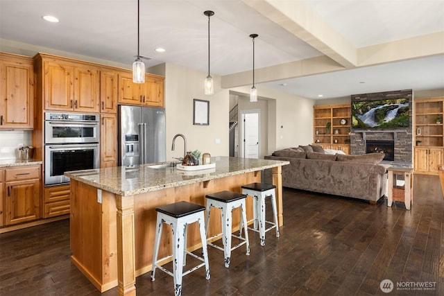 kitchen with light stone counters, a stone fireplace, appliances with stainless steel finishes, dark wood-style floors, and a sink