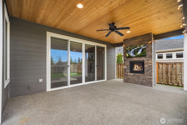 view of patio featuring a lit fireplace, ceiling fan, and fence