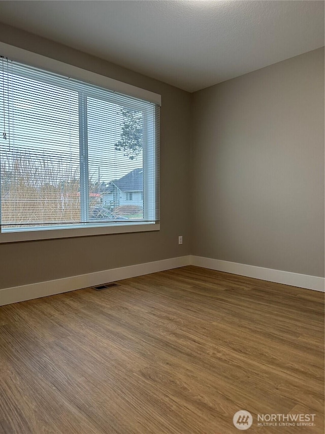 empty room featuring visible vents, baseboards, and wood finished floors