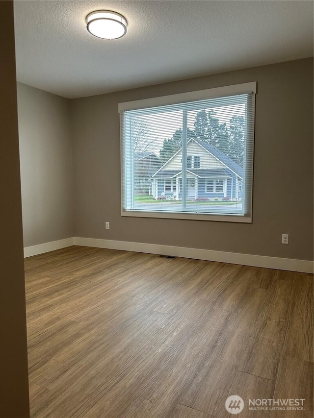 unfurnished room with baseboards, a textured ceiling, and wood finished floors