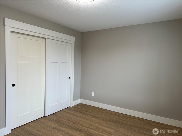 unfurnished bedroom featuring dark wood finished floors, baseboards, a closet, and a textured ceiling