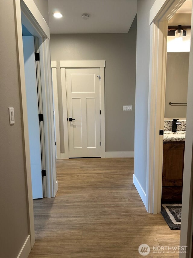 corridor with a sink, recessed lighting, baseboards, and wood finished floors