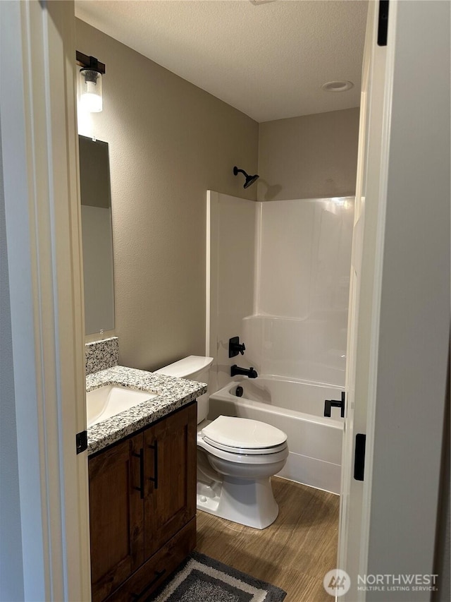 bathroom featuring toilet, shower / tub combination, a textured ceiling, wood finished floors, and vanity