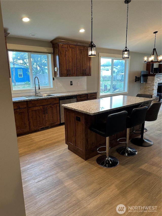 kitchen with light wood-type flooring, a sink, tasteful backsplash, stainless steel dishwasher, and light stone countertops