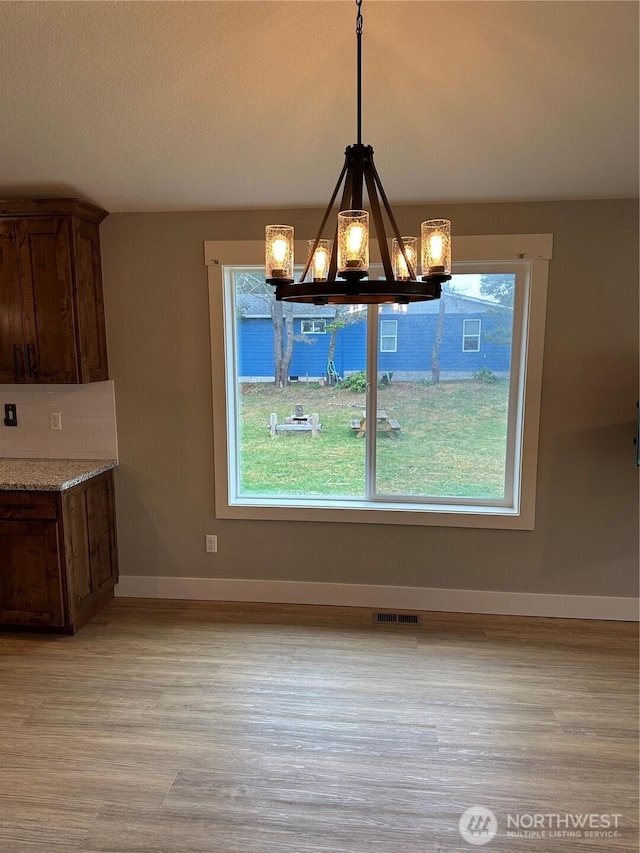 unfurnished dining area with visible vents, a notable chandelier, a textured ceiling, light wood-style floors, and baseboards