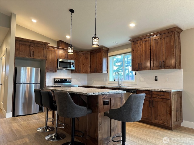 kitchen featuring lofted ceiling, a sink, appliances with stainless steel finishes, a kitchen breakfast bar, and a center island