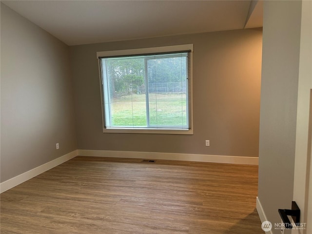 spare room with baseboards and wood finished floors