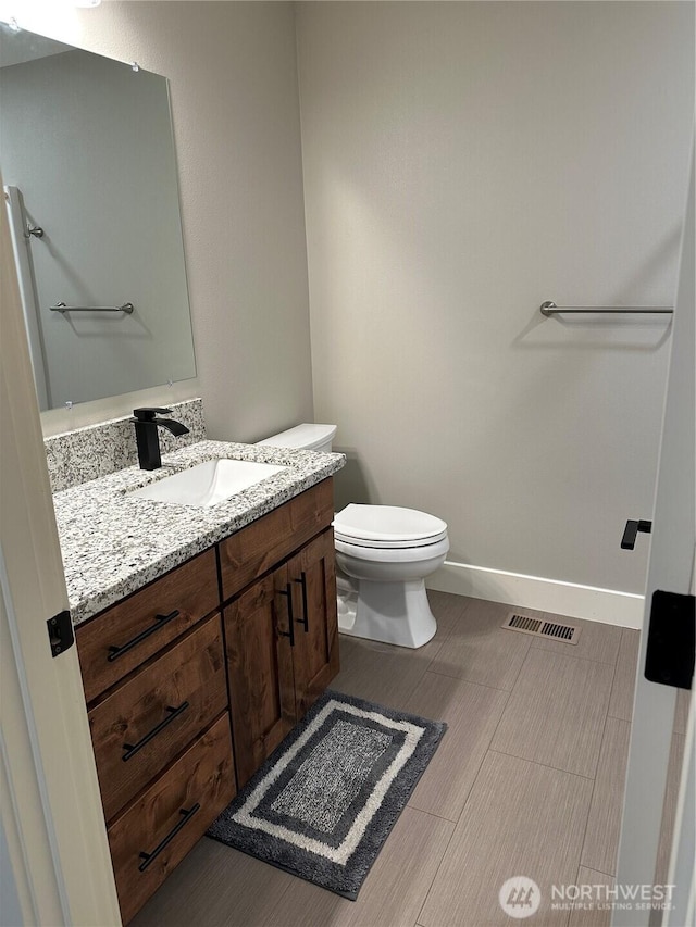 bathroom featuring visible vents, baseboards, toilet, and vanity