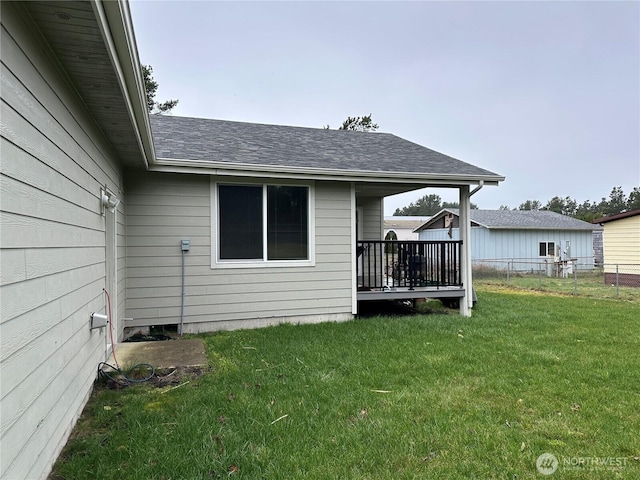 back of property featuring a wooden deck, a lawn, a shingled roof, and fence