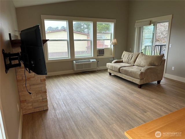 living area with lofted ceiling, baseboards, light wood-type flooring, and a wall mounted air conditioner