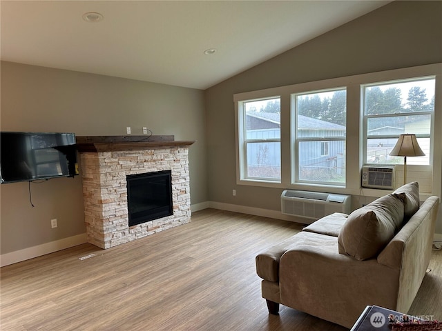 living room with lofted ceiling, an AC wall unit, light wood-style floors, a fireplace, and baseboards