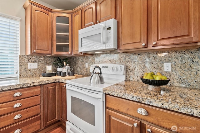 kitchen with light stone counters, glass insert cabinets, white appliances, and tasteful backsplash