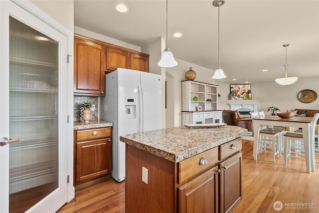 kitchen featuring backsplash, light wood-style floors, white refrigerator with ice dispenser, and pendant lighting