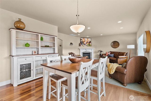 dining room featuring light wood-style flooring, recessed lighting, baseboards, and a premium fireplace