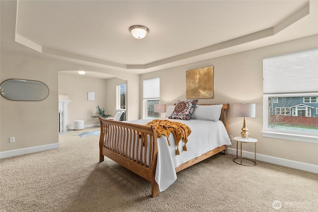 bedroom featuring a tray ceiling, a fireplace with flush hearth, baseboards, and carpet floors