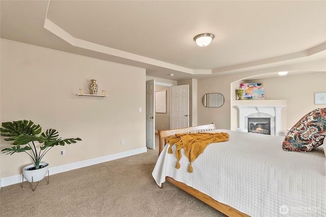 bedroom with baseboards, carpet, a raised ceiling, and a glass covered fireplace