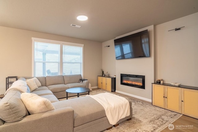 living room with visible vents, baseboards, a glass covered fireplace, and light wood-style flooring