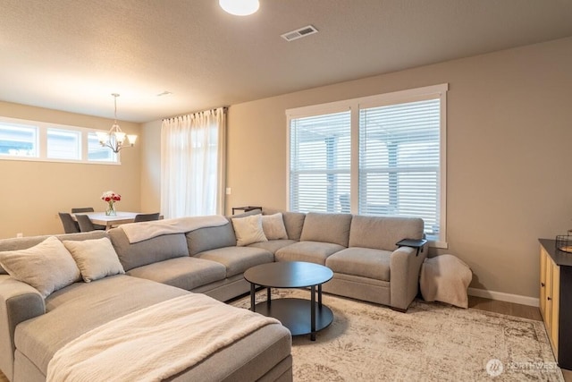 living room with wood finished floors, baseboards, visible vents, a textured ceiling, and a notable chandelier