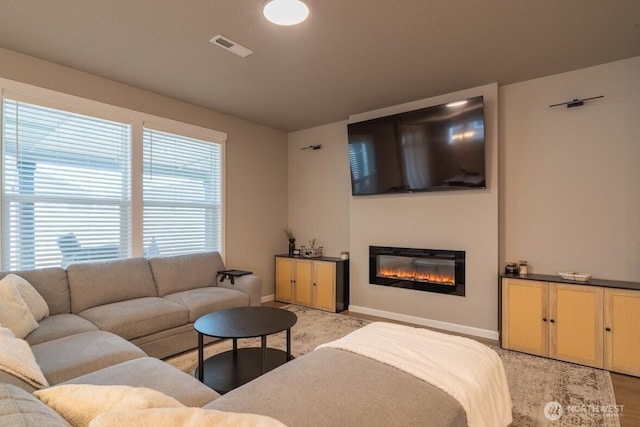 living room with light wood finished floors, a glass covered fireplace, baseboards, and visible vents