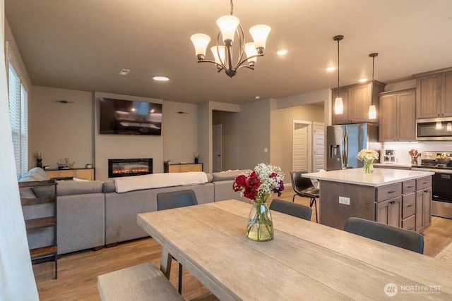 dining room with a glass covered fireplace, light wood-style flooring, recessed lighting, and a chandelier