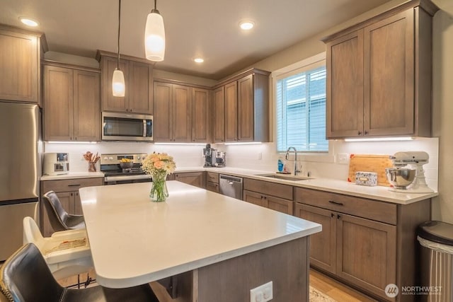 kitchen featuring a kitchen island, a breakfast bar, a sink, stainless steel appliances, and pendant lighting