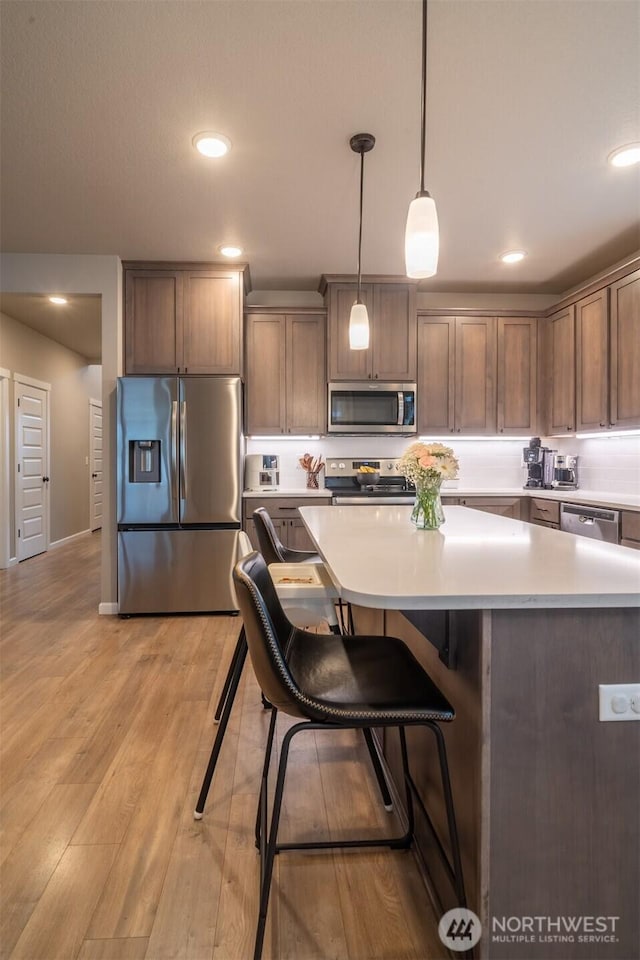 kitchen featuring decorative light fixtures, light countertops, recessed lighting, light wood-style flooring, and stainless steel appliances