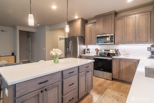 kitchen featuring light countertops, light wood-style flooring, decorative light fixtures, and appliances with stainless steel finishes