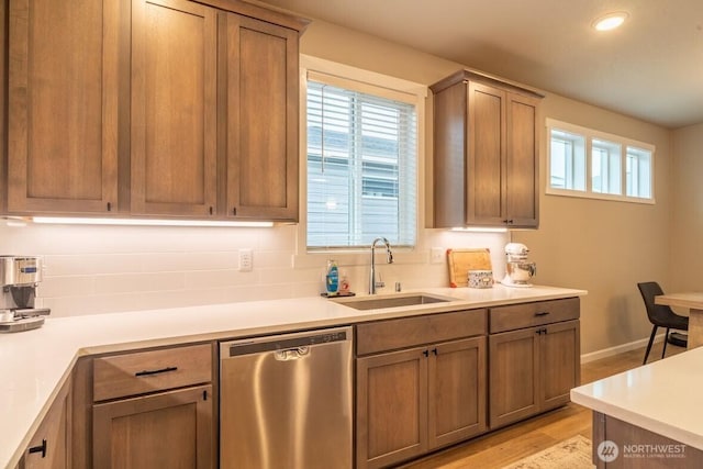 kitchen with brown cabinetry, light wood-style flooring, a sink, light countertops, and dishwasher