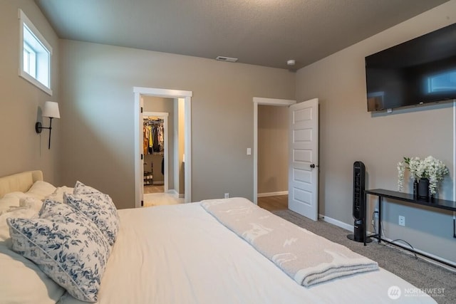 carpeted bedroom with a spacious closet, visible vents, and baseboards