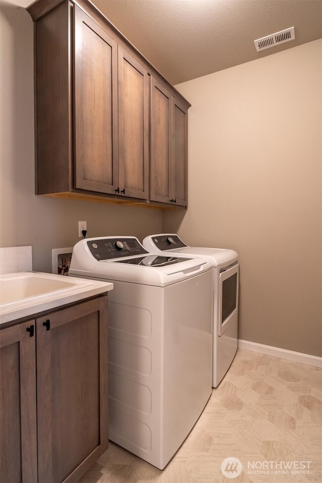 laundry room featuring visible vents, baseboards, separate washer and dryer, cabinet space, and a textured ceiling