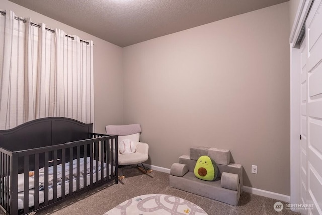 bedroom with a nursery area, carpet, baseboards, and a textured ceiling