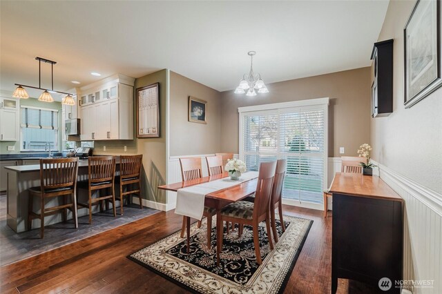 dining room with a notable chandelier, dark wood-style floors, and wainscoting