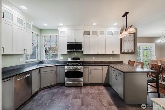 kitchen featuring a peninsula, a sink, appliances with stainless steel finishes, a kitchen bar, and dark countertops