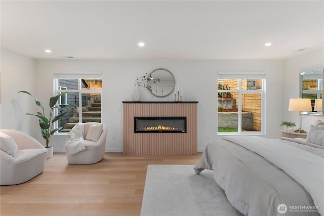 bedroom with a glass covered fireplace, baseboards, wood finished floors, and recessed lighting