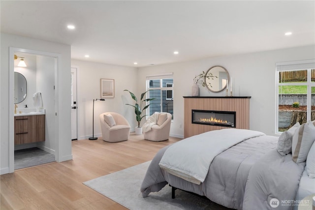 bedroom with a glass covered fireplace, recessed lighting, connected bathroom, light wood finished floors, and baseboards