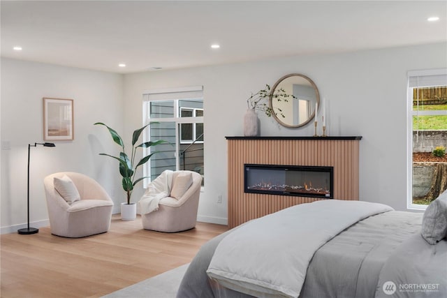 bedroom featuring recessed lighting, baseboards, a glass covered fireplace, and wood finished floors