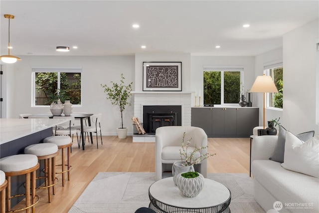 living area featuring recessed lighting, light wood-style flooring, a brick fireplace, and baseboards