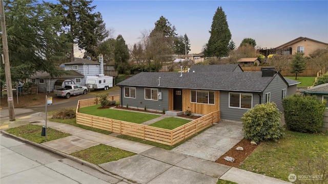 ranch-style house with a fenced front yard, driveway, roof with shingles, and a front lawn