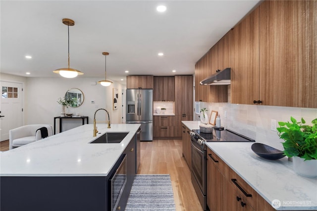 kitchen featuring modern cabinets, a sink, under cabinet range hood, stainless steel appliances, and brown cabinetry