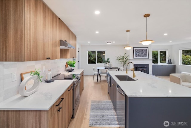 kitchen featuring a sink, under cabinet range hood, a glass covered fireplace, stainless steel appliances, and modern cabinets