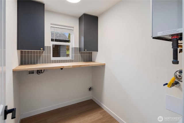 clothes washing area featuring laundry area, light wood-style floors, baseboards, and water heater