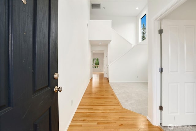 carpeted foyer entrance with visible vents, baseboards, and wood finished floors