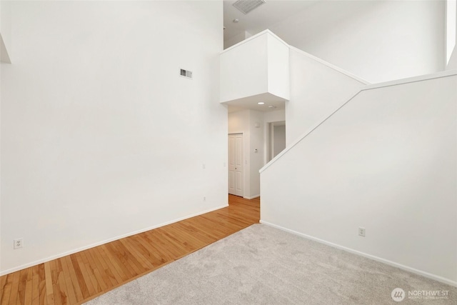 empty room with visible vents, carpet floors, a high ceiling, and baseboards