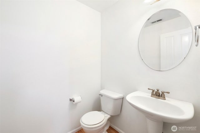 half bathroom with toilet, wood finished floors, baseboards, and a sink