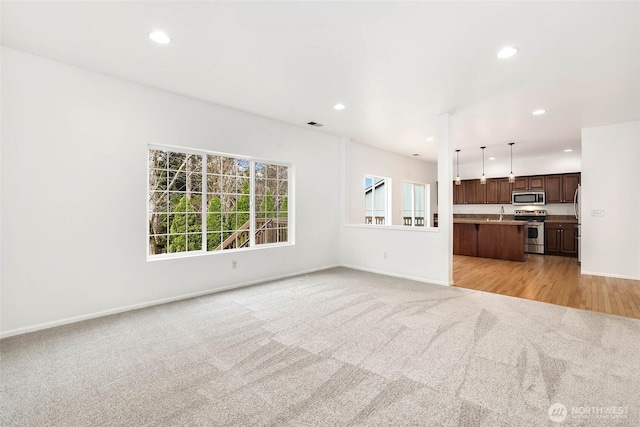 unfurnished living room featuring light carpet, recessed lighting, baseboards, and a wealth of natural light