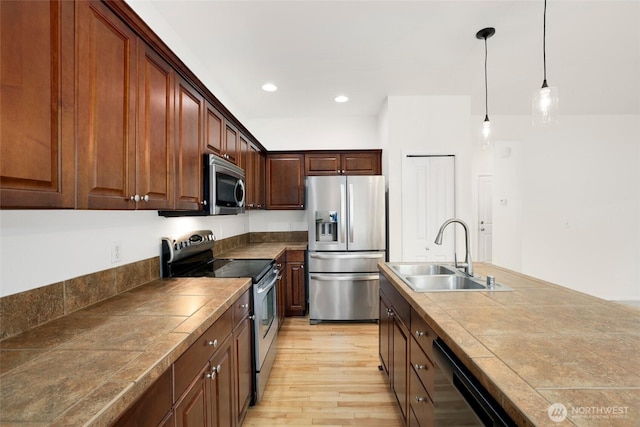 kitchen featuring tile counters, decorative light fixtures, light wood-style flooring, appliances with stainless steel finishes, and a sink